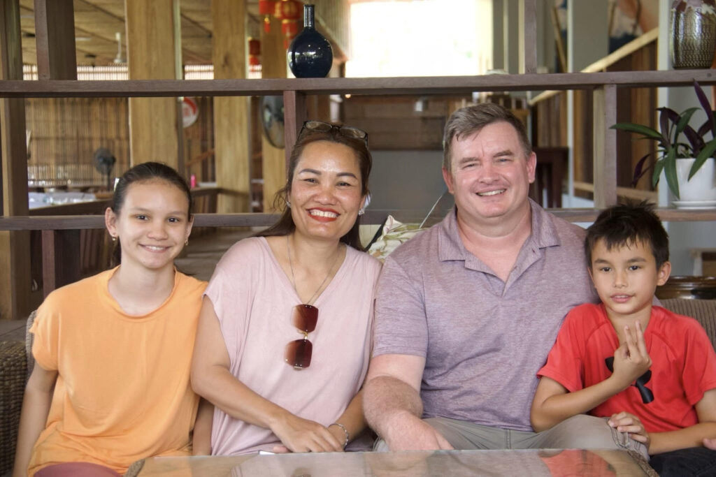 Luke and Sokha Smith sitting with their two children, all smiling at the camera, in a café in Cambodia